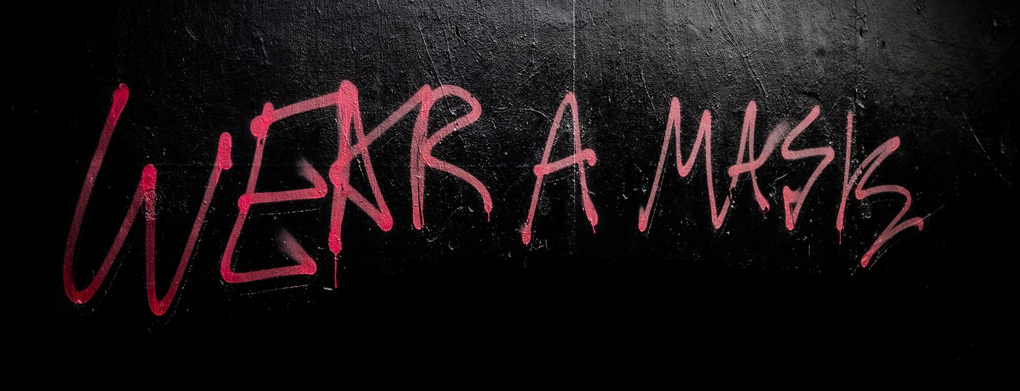 Graffiti that says "Wear a mask" in all caps and red spraypaint, on a black wall