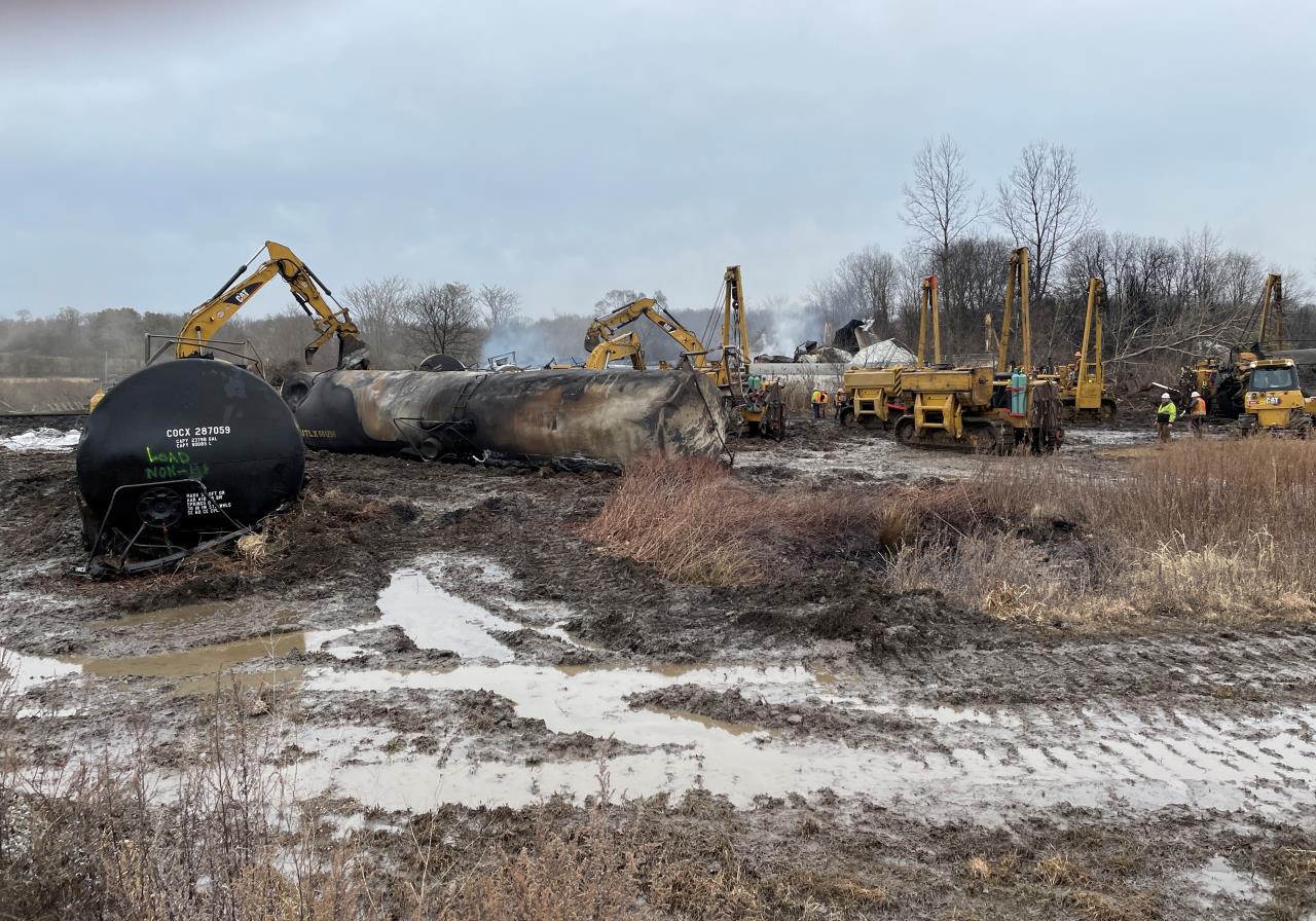 photograph of norfolk southern contractors removing a burned tank car from the crash site.